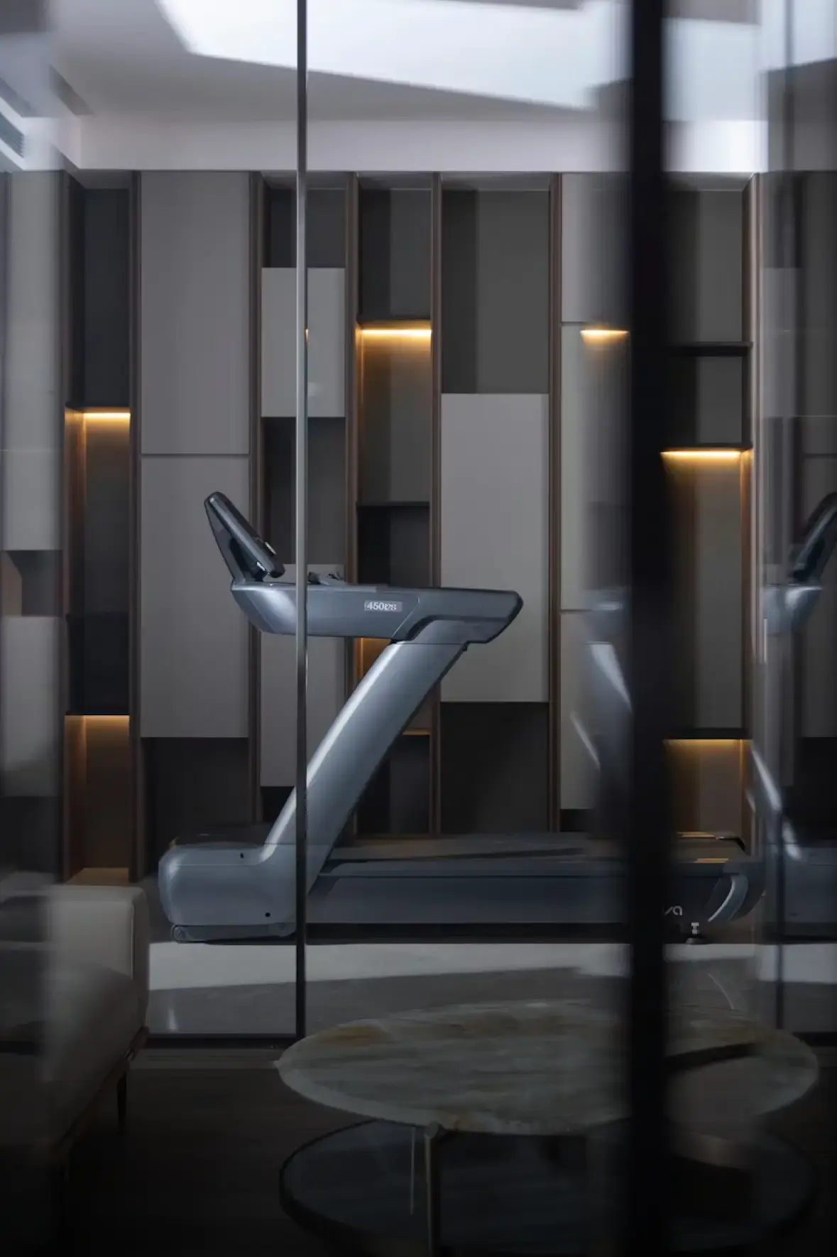 A modern gym space featuring a sleek treadmill in the center, surrounded by stylish, geometric wall panels. The setting feels minimalist and sophisticated.