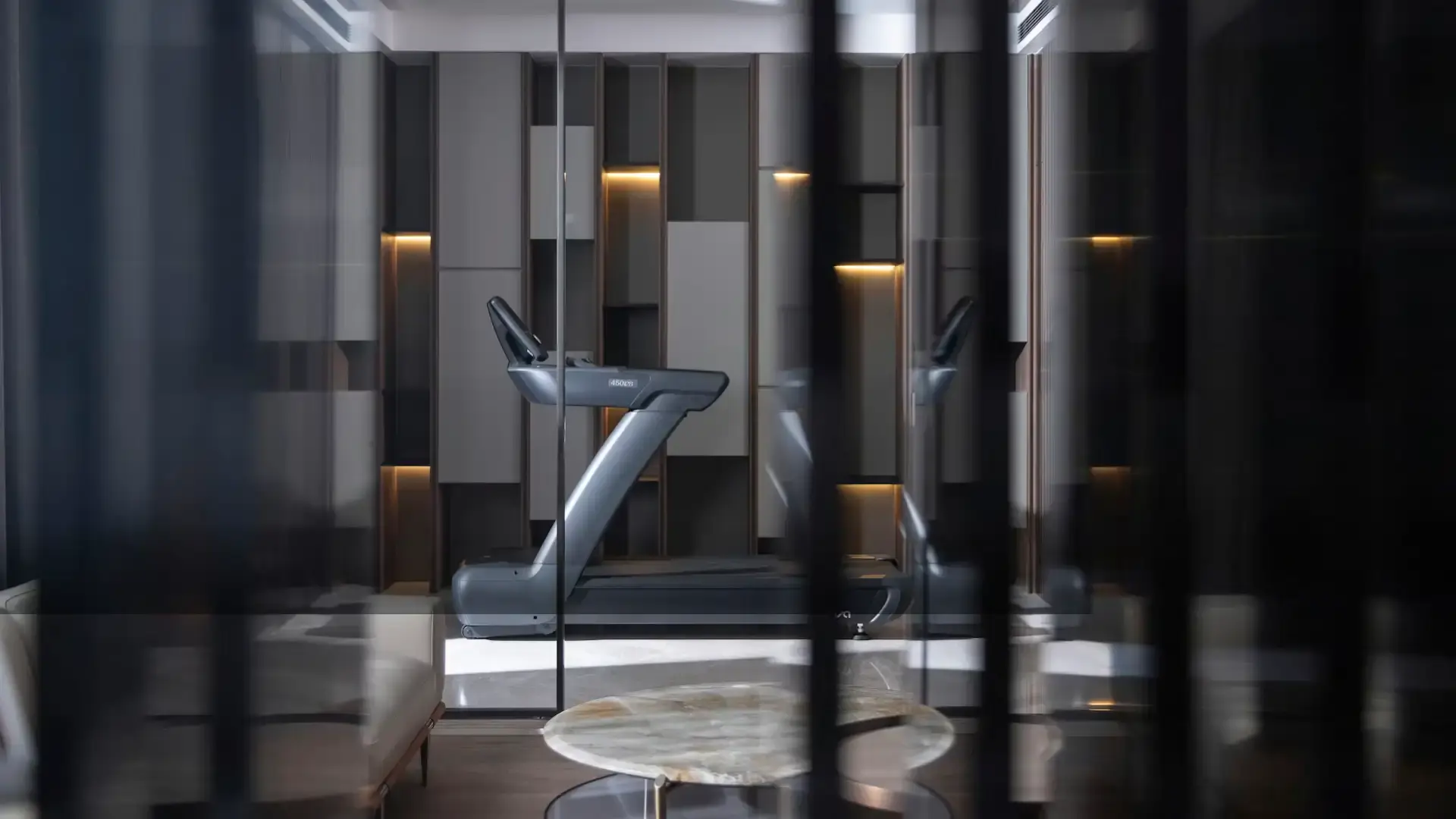 A modern gym space featuring a sleek treadmill in the center, surrounded by stylish, geometric wall panels. The setting feels minimalist and sophisticated.