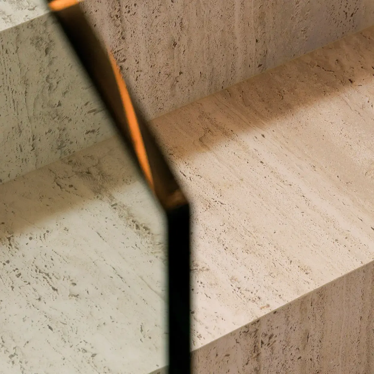 Close-up of travertine stairs with glass railing.