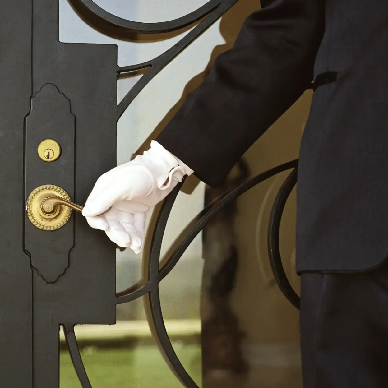 Concierge wearing white gloves opening door.