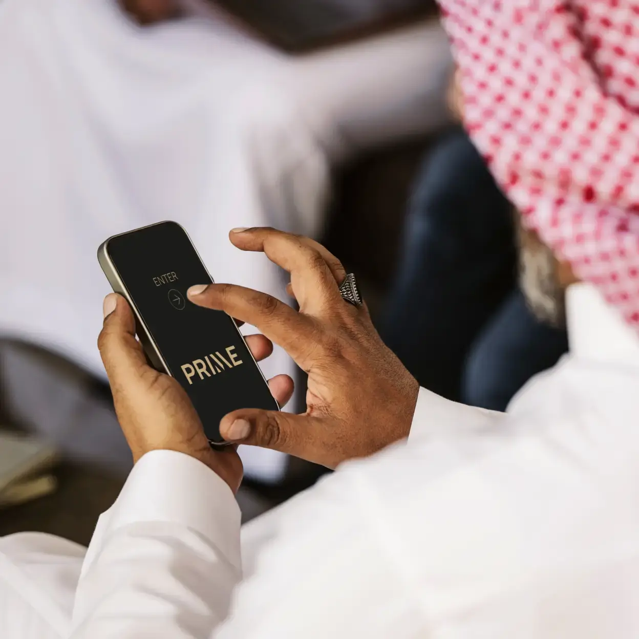 A person wearing traditional attire uses a smartphone displaying the Prime community app