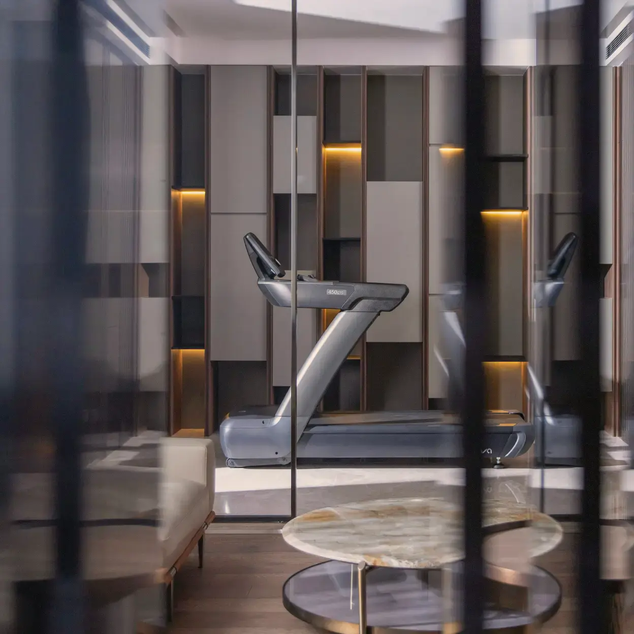 Modern home gym with sleek treadmill against a stylish, geometric wall. Warm lighting creates an elegant, serene atmosphere.