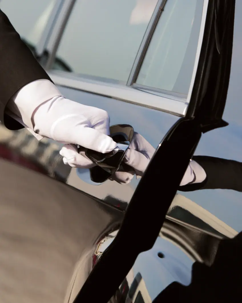 A gloved hand opens a black car door. The reflection on the glossy surface suggests luxury and elegance, creating a formal and attentive mood.