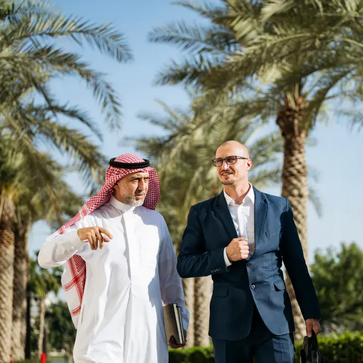 Saudi businessman in traditional attire speaking with a man in a suit outdoors