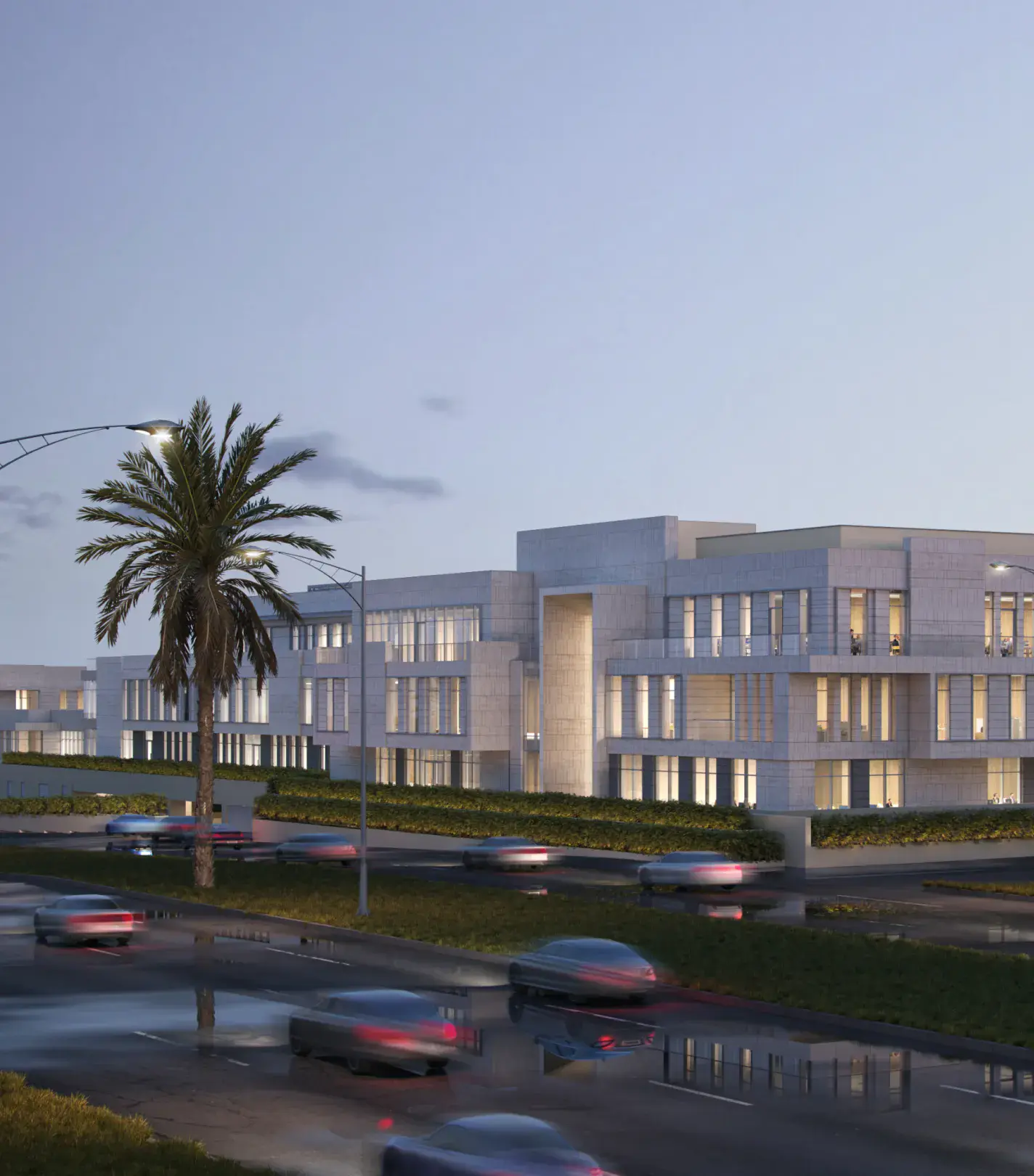 A view of Prime Square and palm trees at dusk as cars drive past.